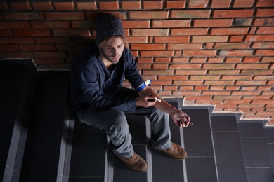Photo of Male drug addict making injection on stairs near brick wall. Space for text