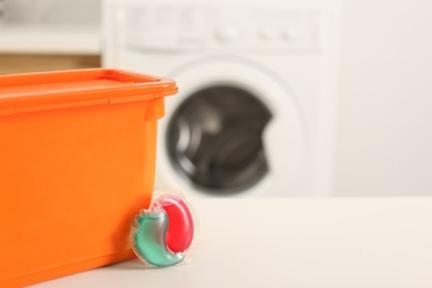 Photo of Laundry container and washing detergent capsule on table indoors. Space for text