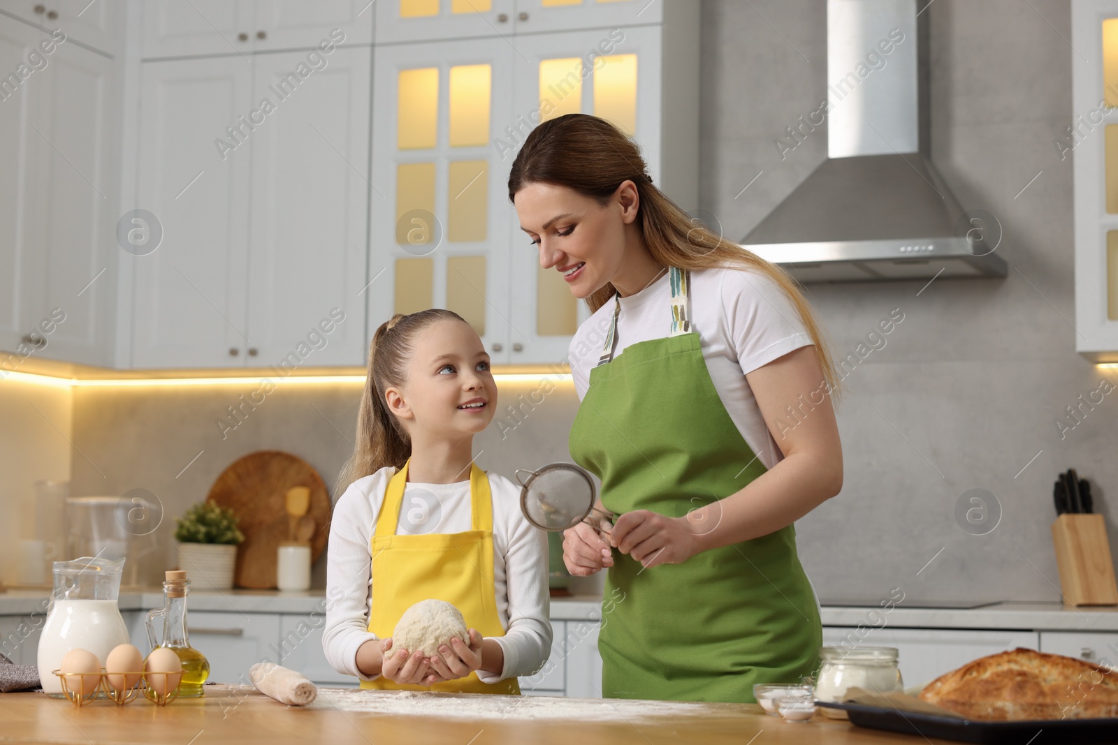 Photo of Making bread. Mother and her daughter kneading dough at wooden table in kitchen