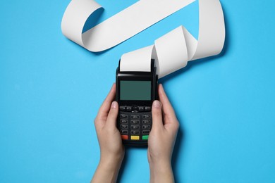 Photo of Woman using payment terminal with thermal paper for receipt on light blue background, top view