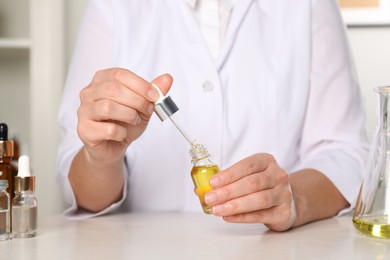 Photo of Dermatologist developing cosmetic oil at white table indoors, closeup