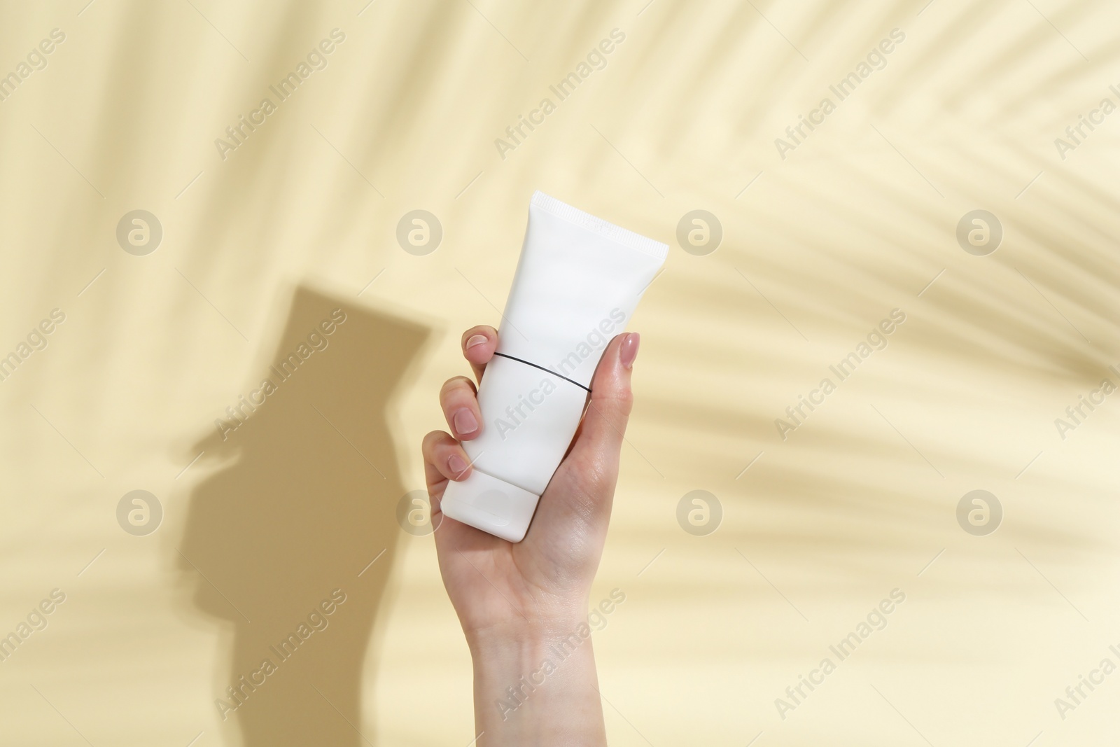 Photo of Woman holding tube of cream on yellow background, closeup