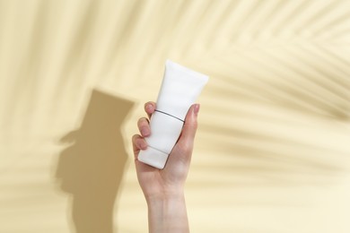 Photo of Woman holding tube of cream on yellow background, closeup