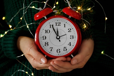 Photo of Woman with alarm clock and festive lights, closeup. New Year countdown