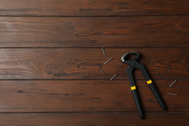Photo of Pincers and nails on wooden background, flat lay with space for text. Carpenter's tool