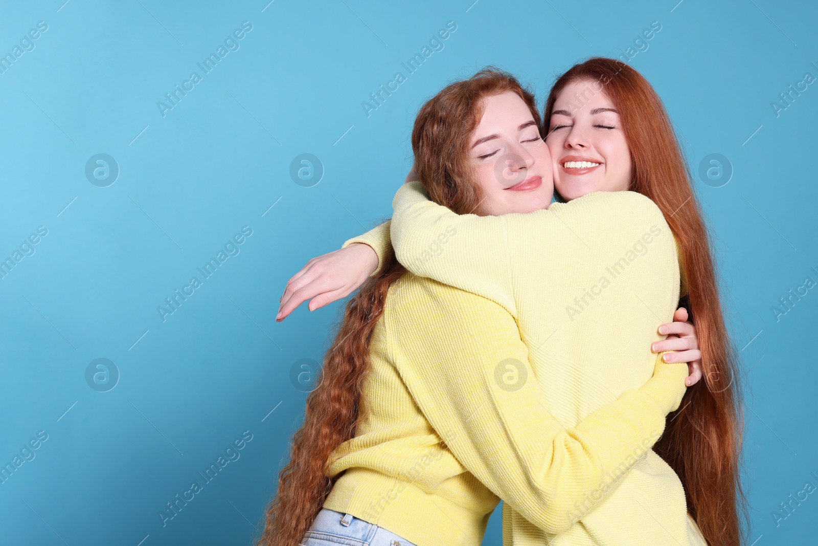 Photo of Portrait of beautiful young redhead sisters on light blue background. Space for text