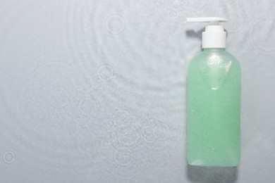 Bottle of facial cleanser in water against light grey background, top view. Space for text