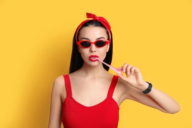 Fashionable young woman in pin up outfit chewing bubblegum on yellow background