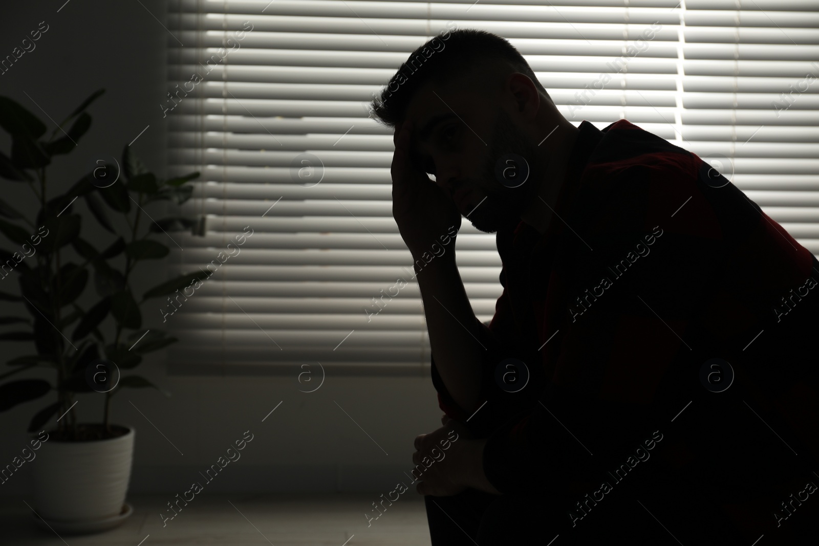 Photo of Silhouette of sad man near closed blinds indoors. Space for text