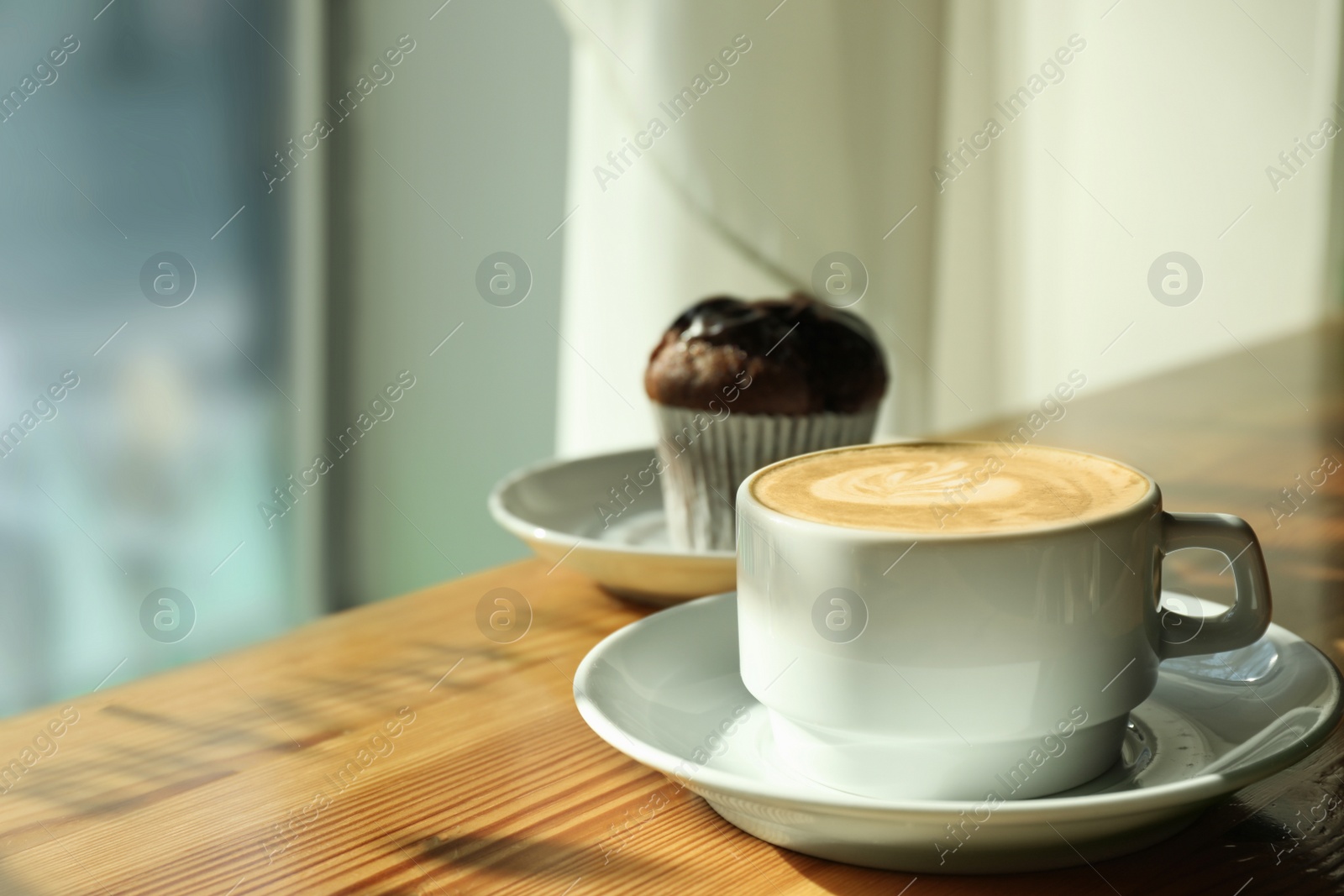 Photo of Cup of fresh aromatic coffee and cupcake at table in cafe