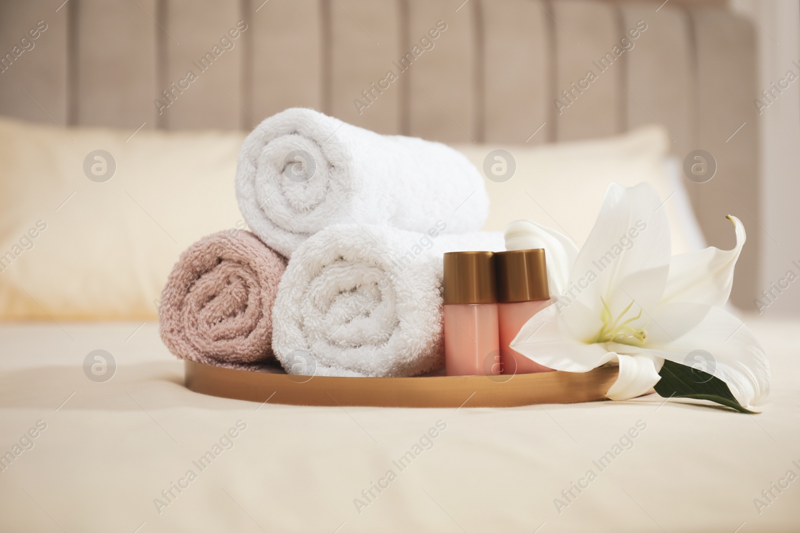Photo of Rolled clean towels, flower and shampoo bottles on bed