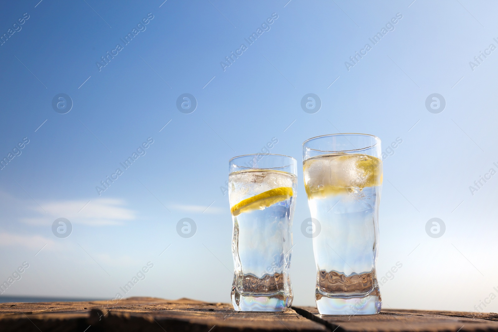 Photo of Wooden table with glasses of refreshing lemon drink on hot summer day outdoors, space for text