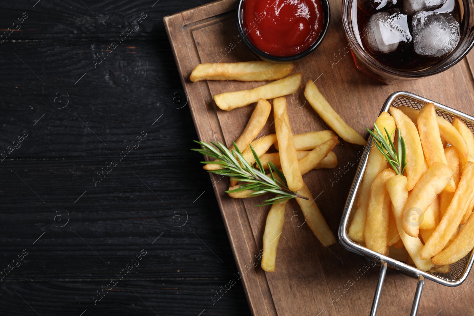 Photo of Tasty french fries, ketchup and soda drink on dark wooden table, top view. Space for text