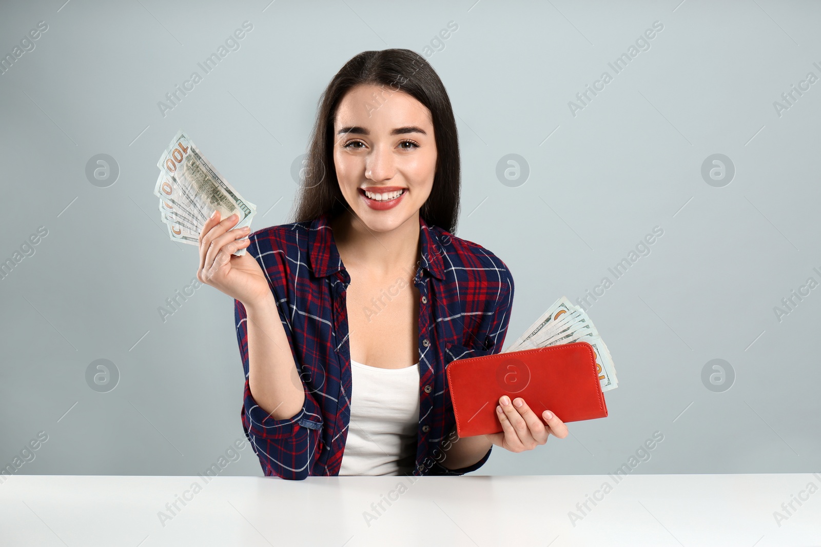 Photo of Young woman with money and wallet at table on light grey background