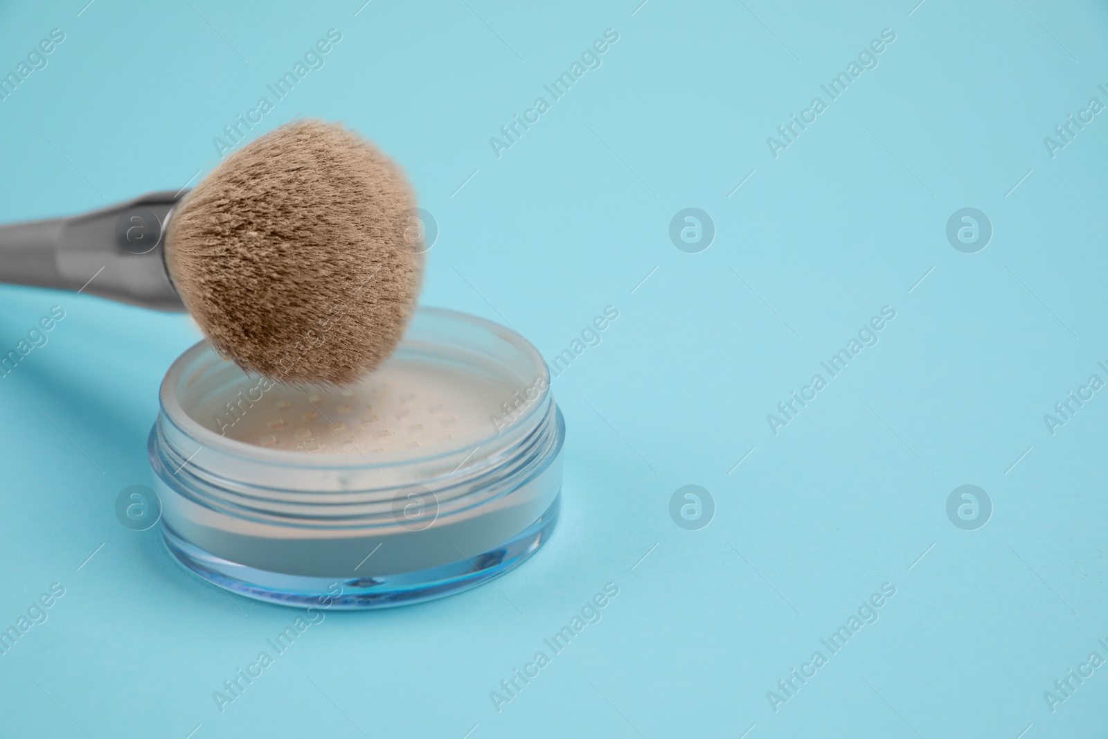 Photo of Loose face powder and brush on light blue background, space for text