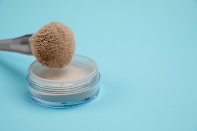 Photo of Loose face powder and brush on light blue background, space for text