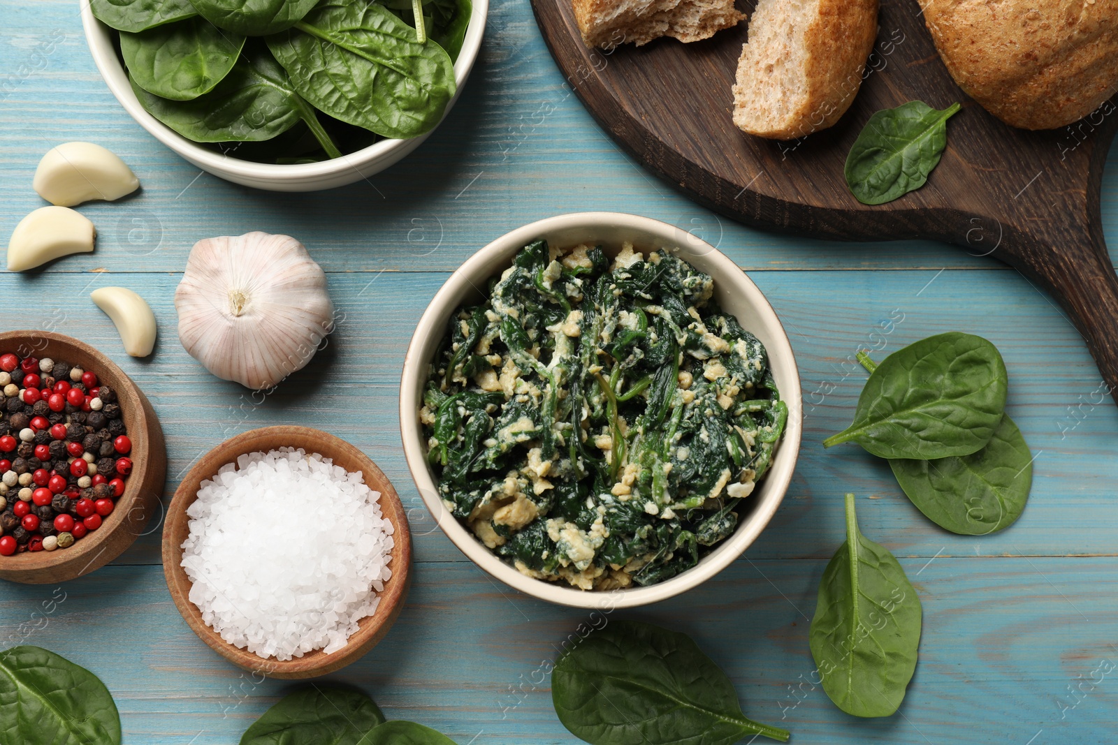 Photo of Tasty spinach dip with egg in bowl, bread and spices on light blue wooden table, flat lay