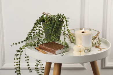 Photo of Burning candles, notebook and houseplant on white wooden table indoors