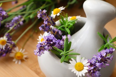 Photo of Mortar with fresh lavender, chamomile flowers, rosemary and pestle on table, closeup