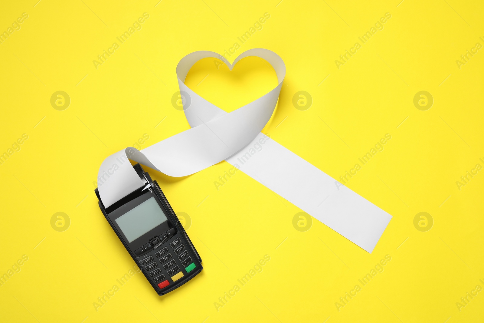 Photo of Payment terminal and heart made of thermal paper for receipt on yellow background, top view