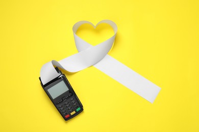 Payment terminal and heart made of thermal paper for receipt on yellow background, top view