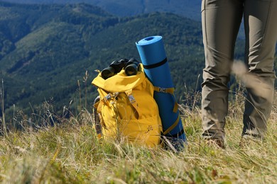Photo of Tourist with backpack, sleeping pad and binoculars in mountains on sunny day, closeup