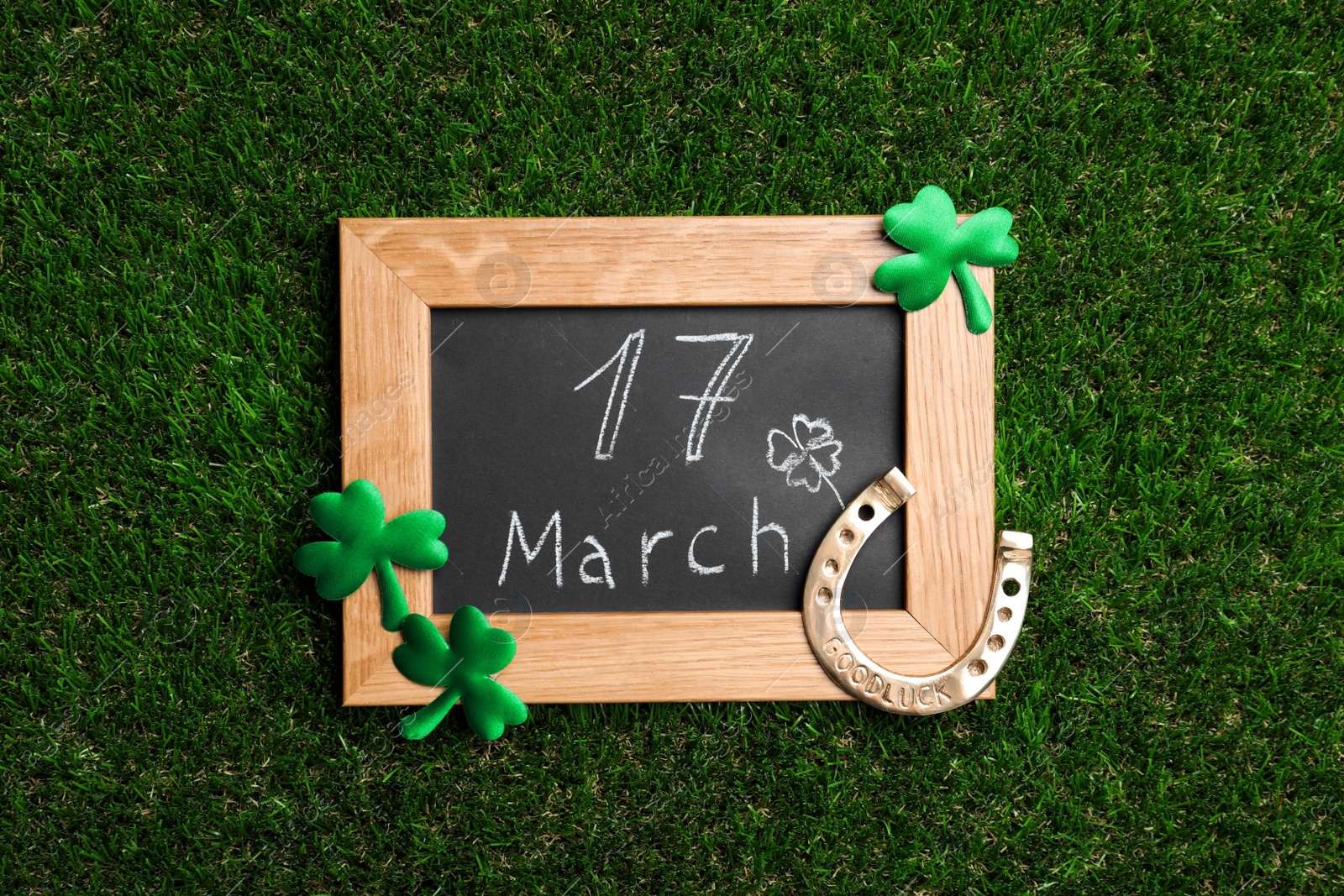 Photo of Flat lay composition with horseshoe and chalkboard on grass. St. Patrick's Day celebration