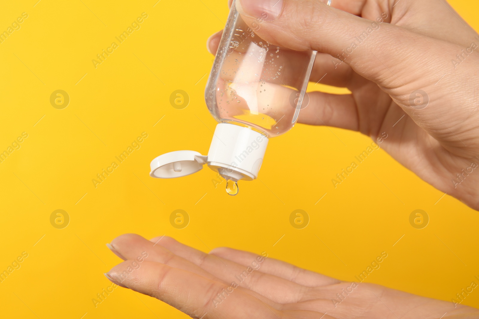 Photo of Woman applying antiseptic gel on yellow background, closeup