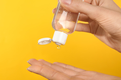 Photo of Woman applying antiseptic gel on yellow background, closeup