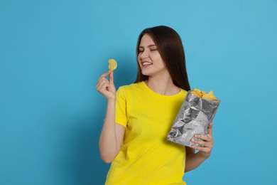 Photo of Pretty young woman with bag of tasty potato chips on light blue background