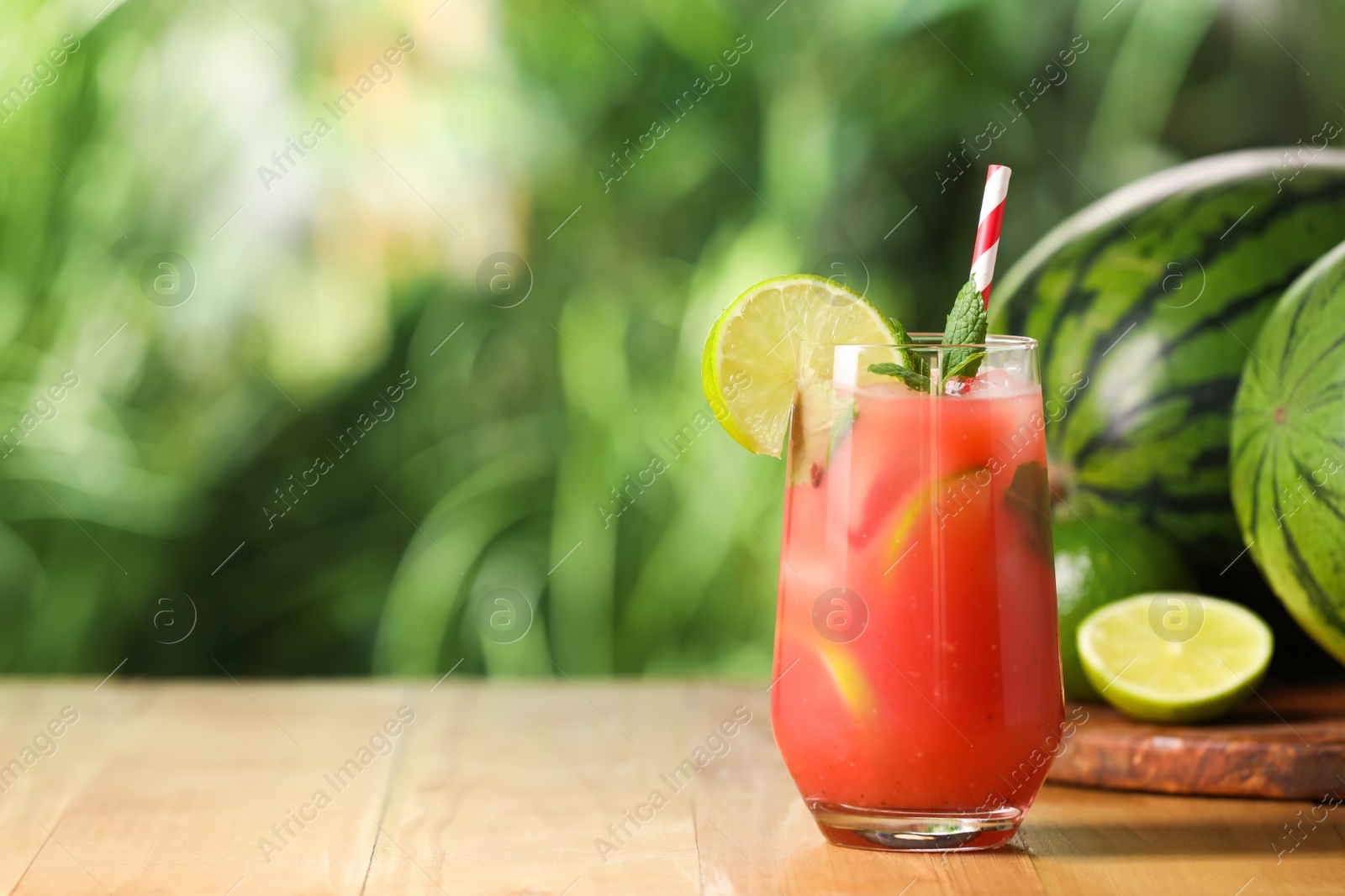 Photo of Glass of freshly made watermelon juice with lime and mint on wooden table outdoors, space for text