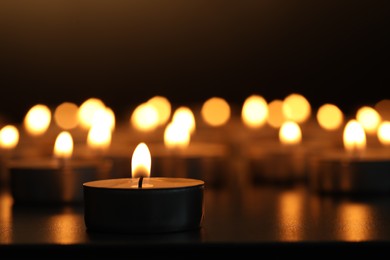 Burning candles on dark surface against black background, closeup. Space for text