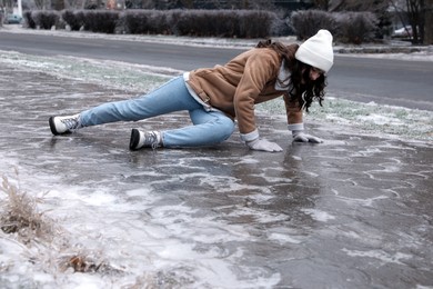 Young woman trying to stand up after falling on slippery icy pavement outdoors