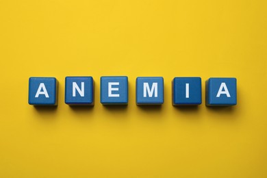 Photo of Word Anemia made with blue wooden cubes on yellow background, flat lay