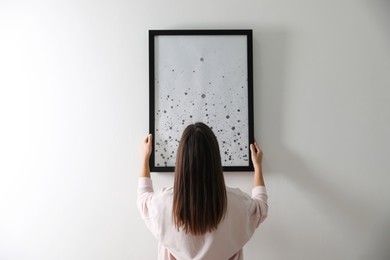 Photo of Woman hanging picture on white wall indoors