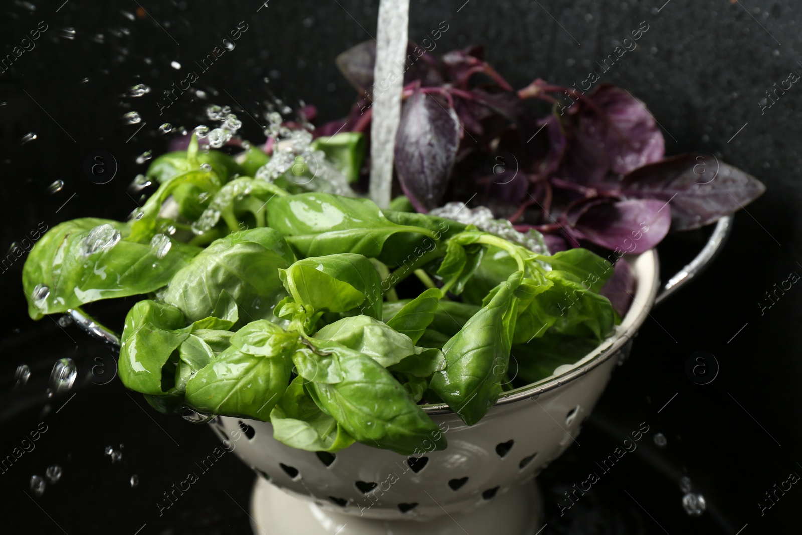 Photo of Washing different fresh basil leaves under tap water in metal colander in sink, closeup