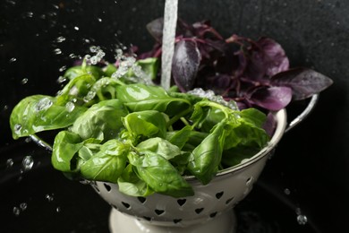 Photo of Washing different fresh basil leaves under tap water in metal colander in sink, closeup