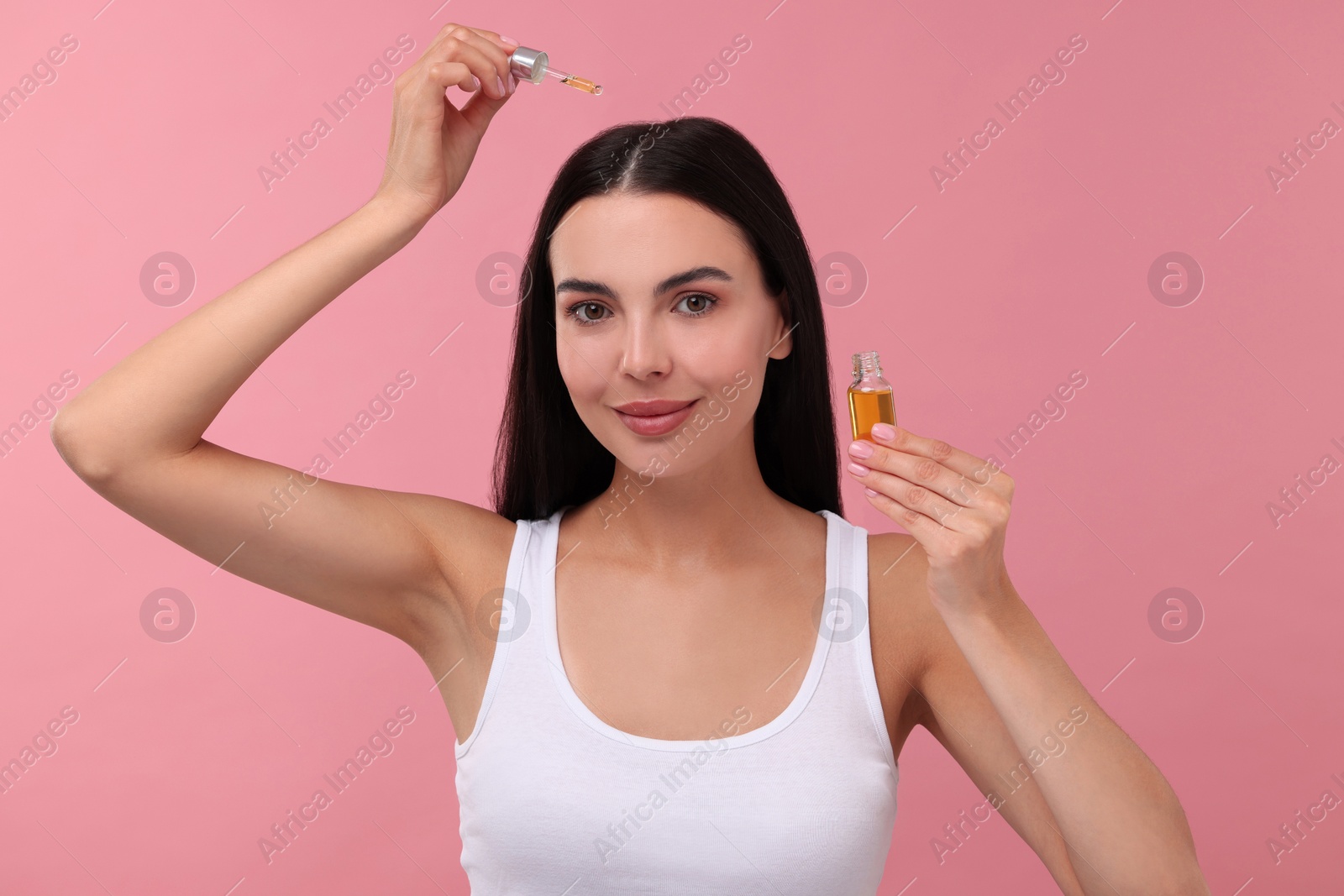 Photo of Beautiful woman applying hair serum on pink background. Cosmetic product