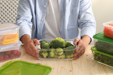 Man holding glass container with fresh broccoli at wooden table, closeup. Food storage