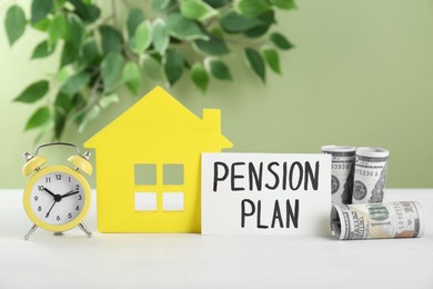 Card with phrase Pension Plan, dollar banknotes, yellow house figure and alarm clock on white wooden table. Retirement concept