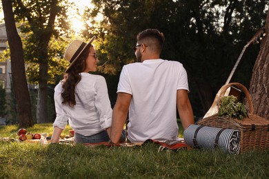 Photo of Lovely couple having picnic on plaid in summer park, back view