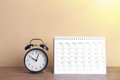 Calendar and alarm clock on wooden table against beige background