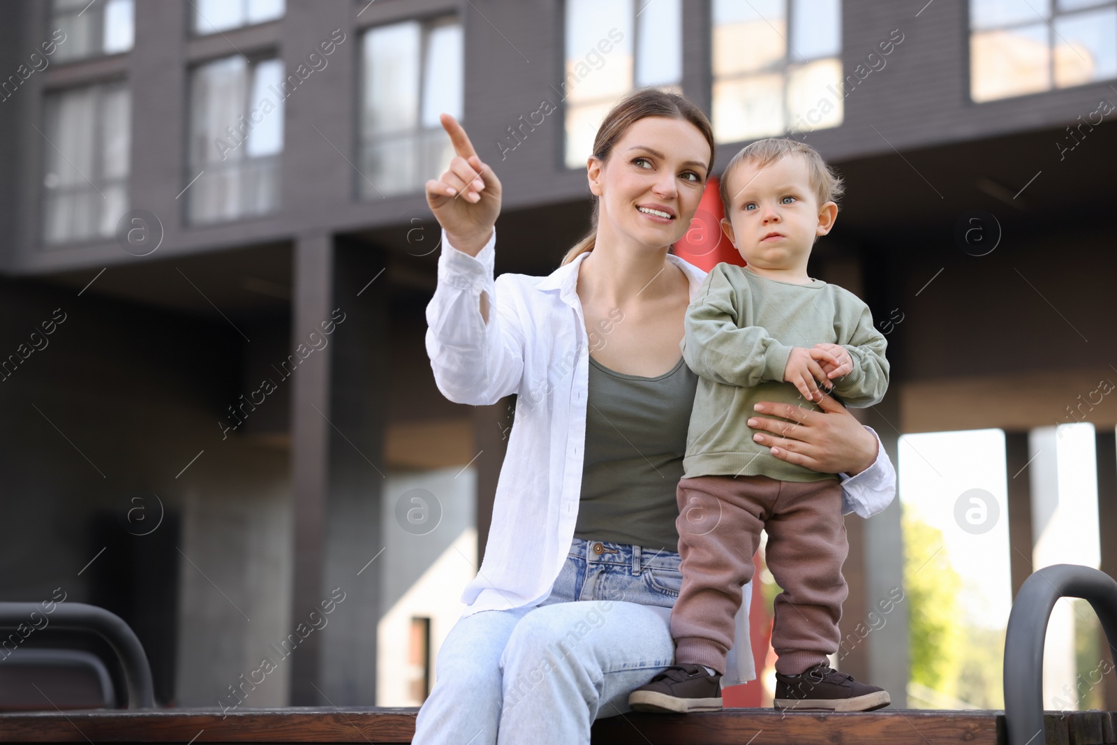 Photo of Happy nanny with cute little boy on bench outdoors, space for text