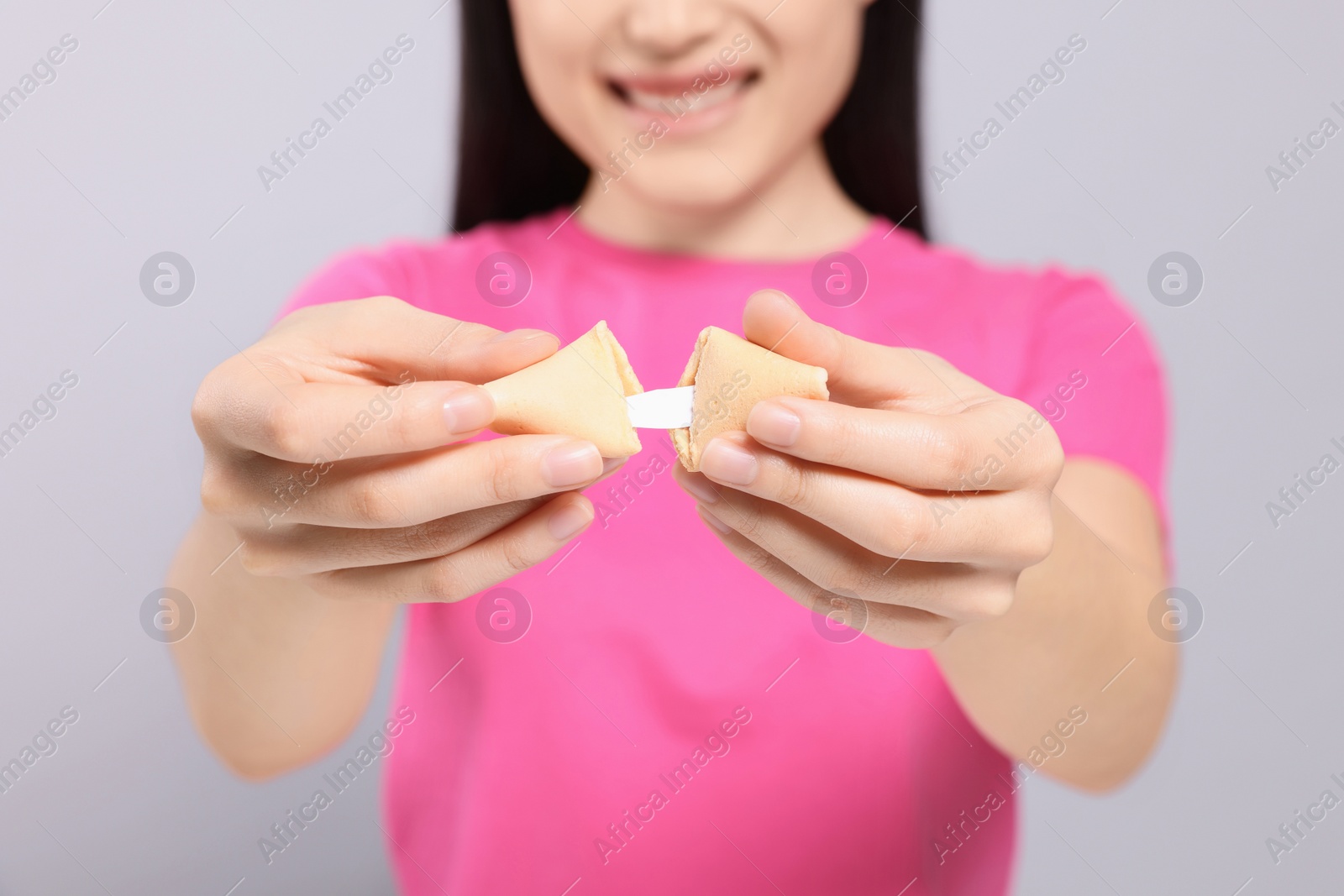 Photo of Young woman holding tasty fortune cookie with prediction on grey background, closeup