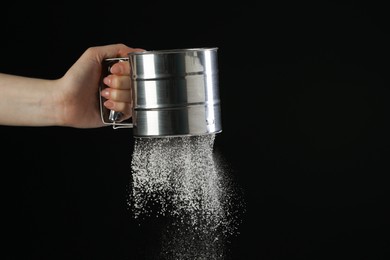Woman sieving flour against black background, closeup. Space for text