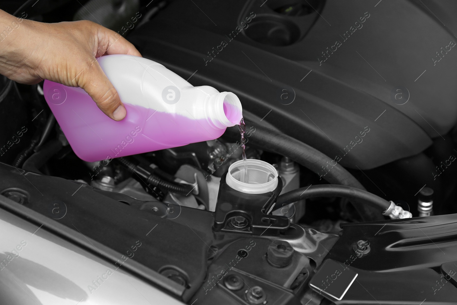 Photo of Man pouring liquid from plastic canister into car washer fluid reservoir, closeup