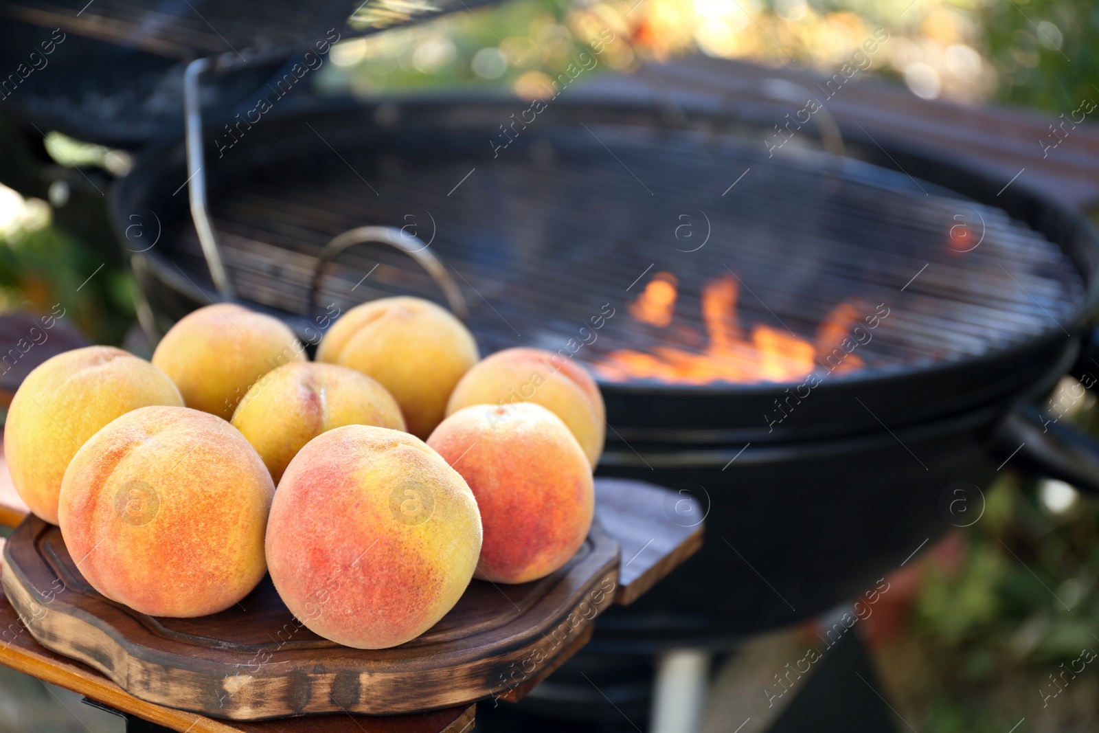 Photo of Fresh peaches on wooden table near modern grill outdoors, closeup