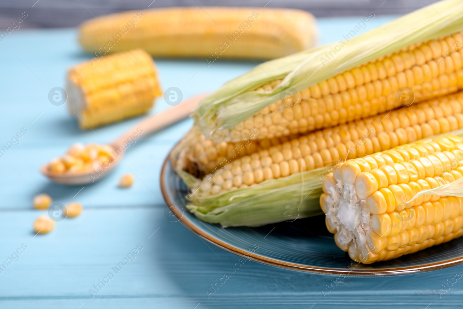 Photo of Plate with tasty sweet corn cobs on wooden table, closeup