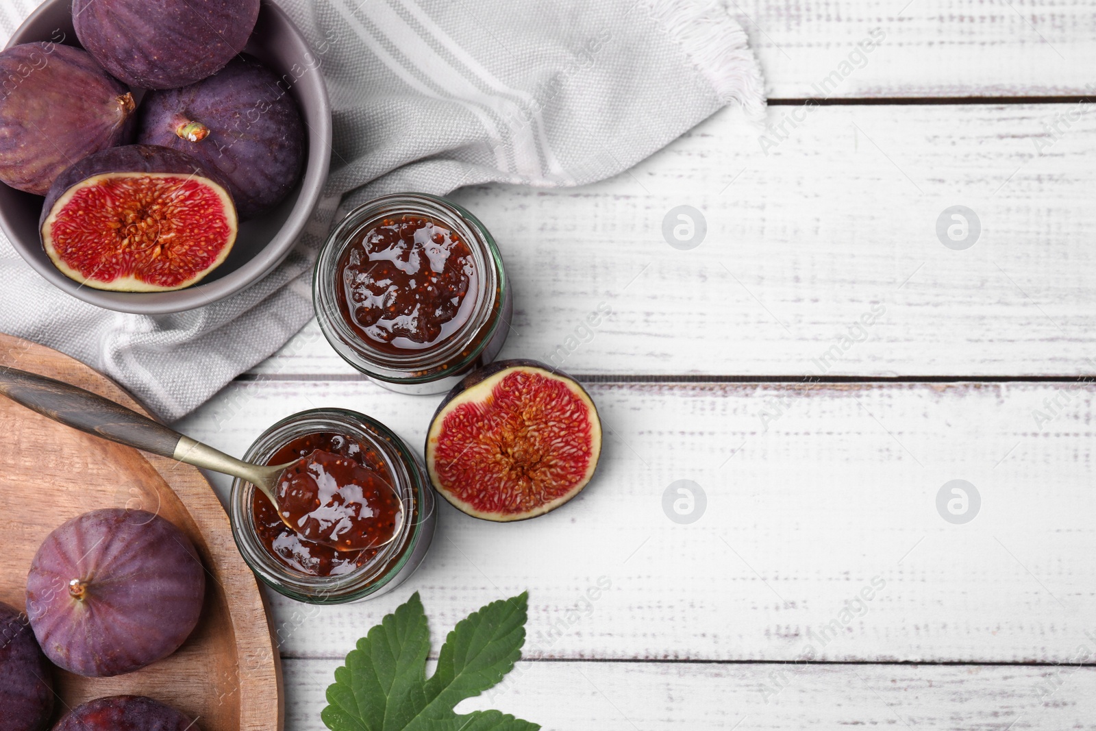 Photo of Glass jars of tasty sweet fig jam and fruits on white wooden table, flat lay. Space for text