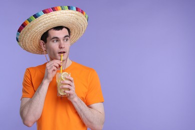 Photo of Young man in Mexican sombrero hat drinking cocktail on violet background. Space for text